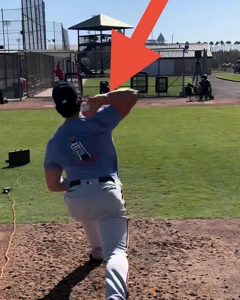 Behind-the-back view of a professional baseball pitcher on a dirt mound during a diagnostic session. A large red arrow points to a high-speed motion capture camera and sensor setup, illustrating the data-driven 'Find the Problem' step of the PRO Athlete PT process